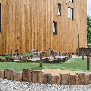 Praktické využití zahradních pražců pro ohraničení minigolfového hřiště u luxusního hotelu, v pozadí budova fasády hotelu obložena fasádním obkladem KI - Trend v okrovém provedení.