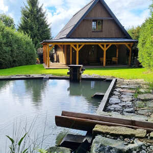 Pohled na rekreačn&iacute; chatu na Lipensku. Chata je obložena dřevěn&yacute;m obkladem KI Trend v &scaron;ed&eacute;m odst&iacute;nu a m&aacute; terasu z terasov&yacute;ch prken KI Duo ve stejn&eacute;m odst&iacute;nu. Technologie olejově-vakuov&eacute; impregnace poskytuje dřevu v exteri&eacute;ru maxim&aacute;ln&iacute; ochranu. 