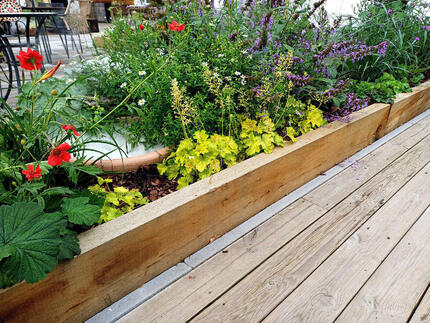 Detail nadzemního záhonu z impregnovaných zahradních pražců a terasy z impregnovaných prken z borovice, oboje Profi impregnace.  Detail nadzemního záhonu z impregnovaných zahradních pražců a terasy z impregnovaných prken z borovice, oboje Profi impregnace.